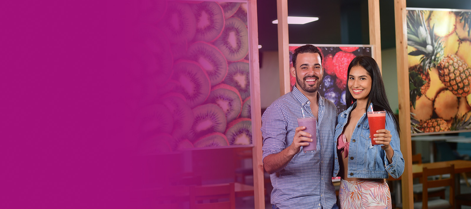 Fotografía de dos personas de pie sosteniendo vasos con jugos elaborados en uno de los locales de Disfruta