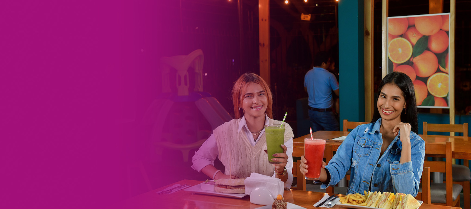 Fotografía de dos personas sentadas sosteniendo vasos con jugos elaborados en uno de los locales de Disfruta